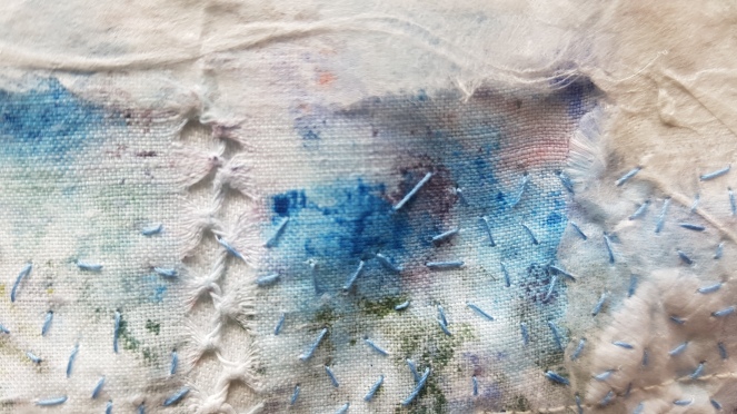 A close up photo of a small fragment of layered, frayed white fabrics and papers tinted with blue, with fine blue seed stitches.